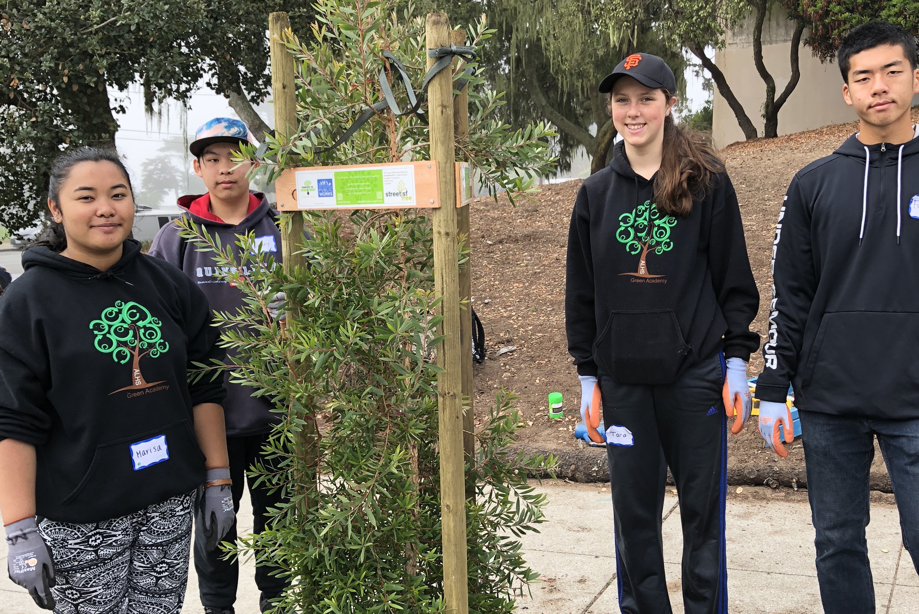 Green Academy students standing by a newly planted tree.