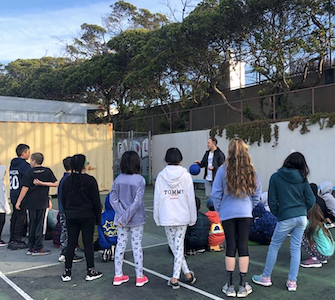 Students grouped around a teacher holding a ball