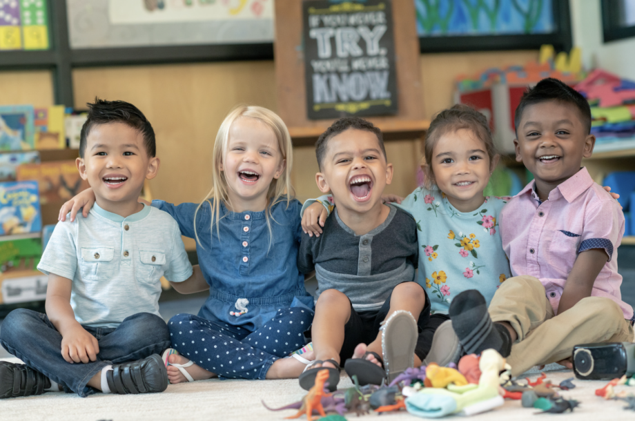 Five children setting on the floor, smiling.