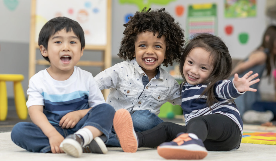 Three preschool-age children (two boys and a girl) sitting on the floor, smiling