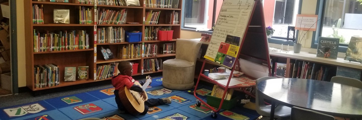 Student playing a guitar on the rug.