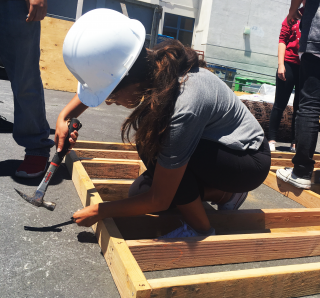 Female high school student hammering wooden frame