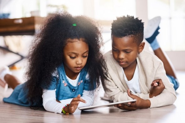 Photo of two children on the floor at home sharing an iPad