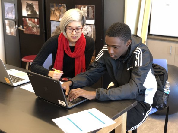 teacher sitting with a student at a laptop