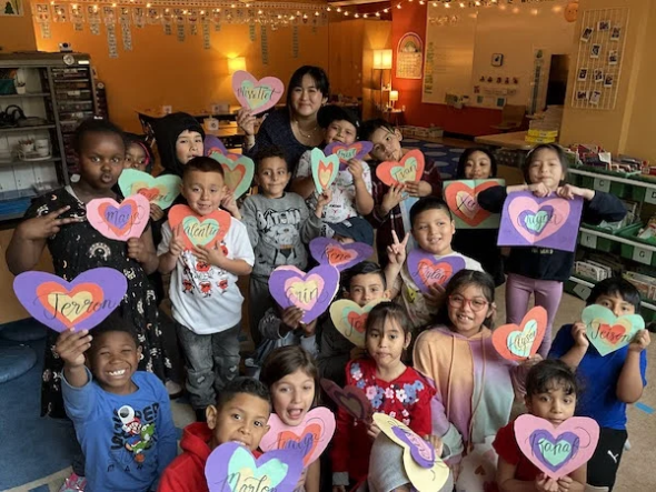 a group of students face the camera and smile while holding paper hearts