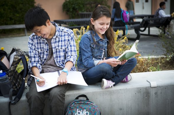 Two students sitting back to back writing in notebooks