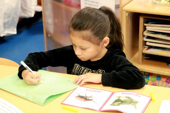 Girl practicing writing with book next to her