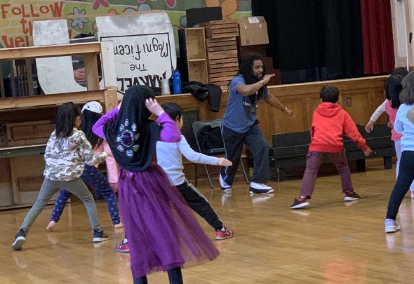 Mr. Jarrel in auditorium with students in capoeira move