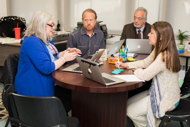 Four teachers with laptops sitting around a table