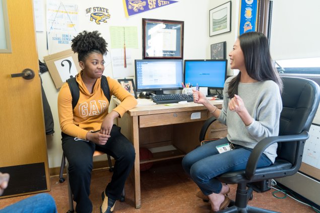 A female student talks to a female adult while both are sitting.