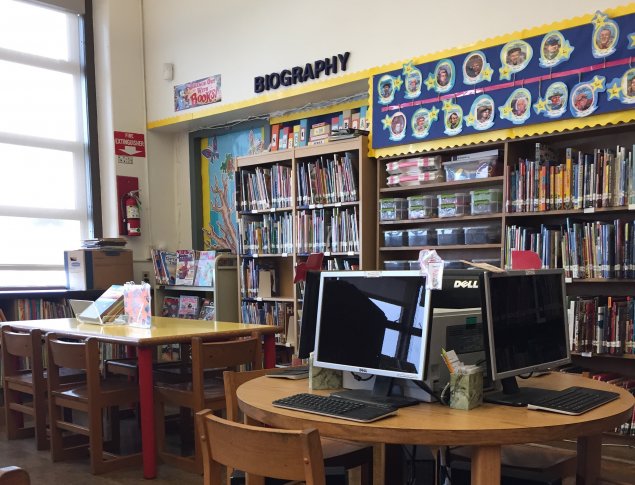 School library with book shelves and computers at a round table in the foreground