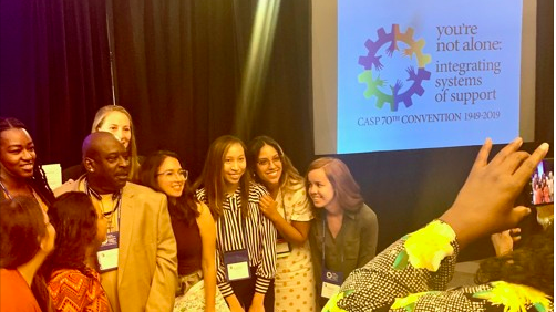 Darryl Lester surrounding by 8 women posing for a picture in front of a presentation screen.