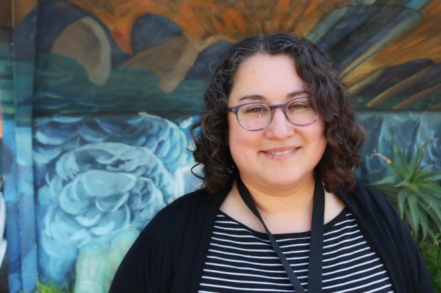 Latina woman with curly hair and glasses.