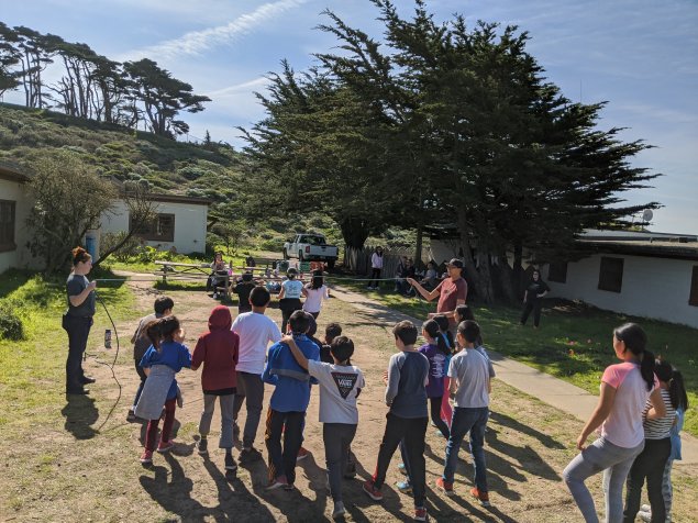 A group of kids running through a jump rope at the park.