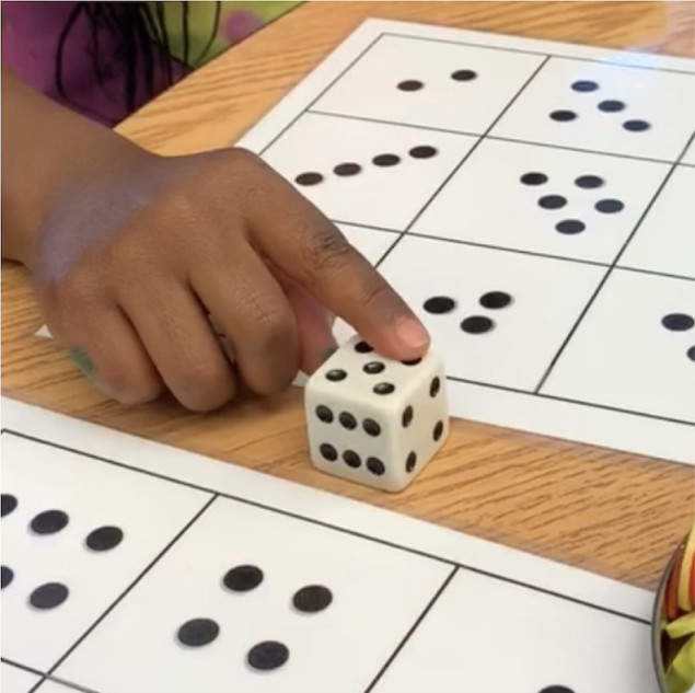 Student touching a die next to mats with die faces.