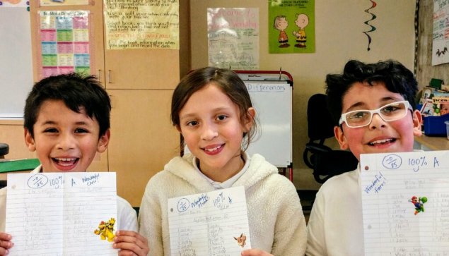 Three students in classroom holding papers