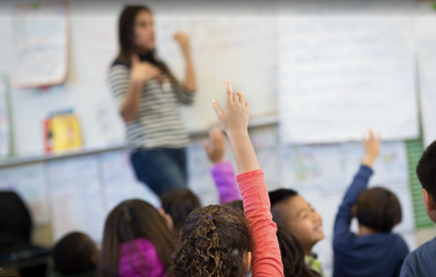 Teacher in classroom with students raising their hands