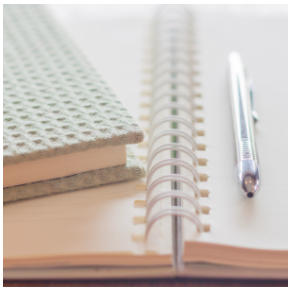 A open empty sketchbook, pen and another journal, all in colors of grey, cream and white