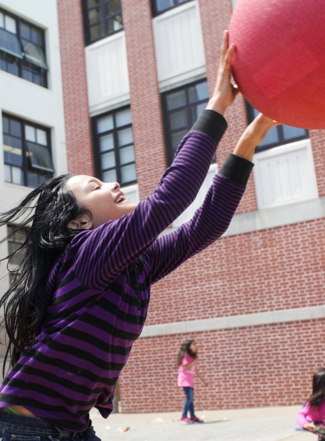 child catching a red ball in front of a red brick building